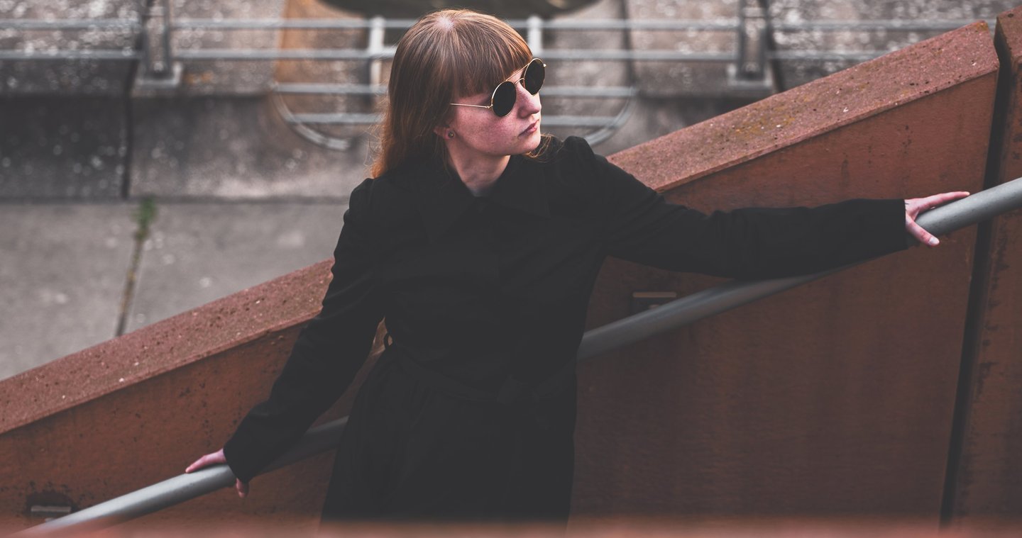 a woman in sunglasses and a black jacket standing on a stair case