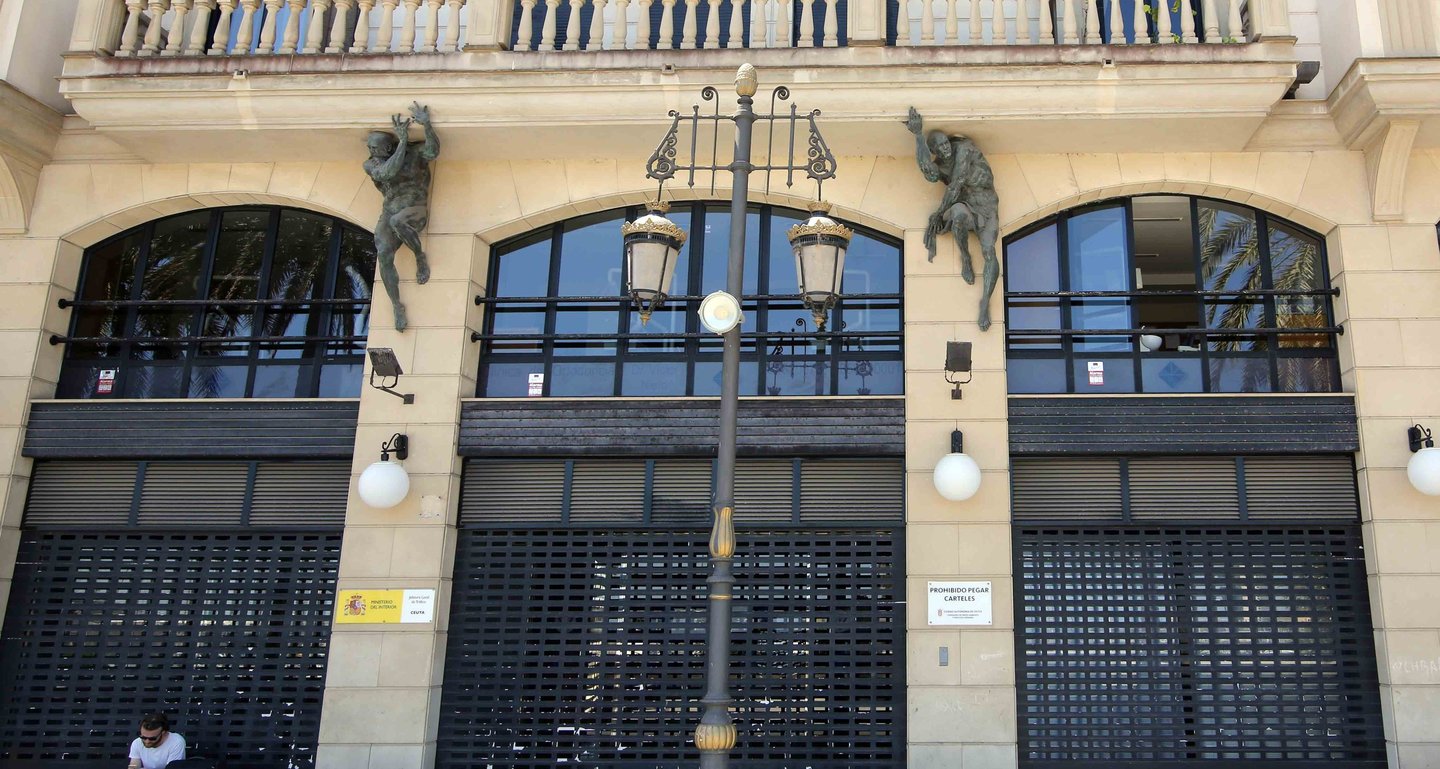 Ornate building facade in Valencia featuring sculptural atlantes and black storefront shutters.
