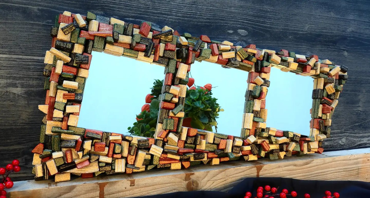 Elegantes Spiegelunikat mit kunstvollem Rahmen aus schwarzen, roten, goldenen und grünen Holzscheiten