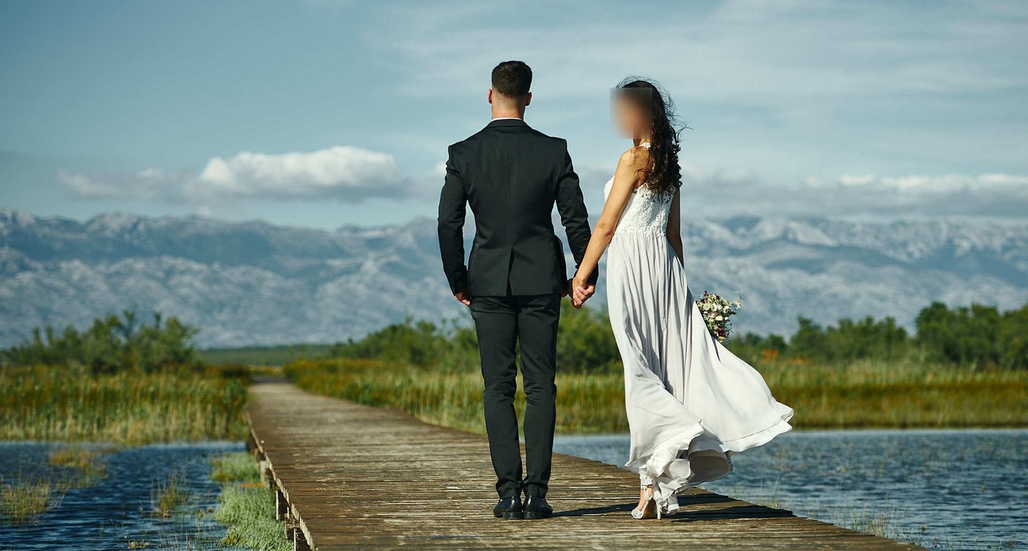The photo shows a wedding couple holding hands in Nin, with Velebit in the background.