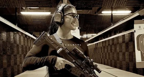 mais alhajri smiling while holding a rifle at an indoor shooting range