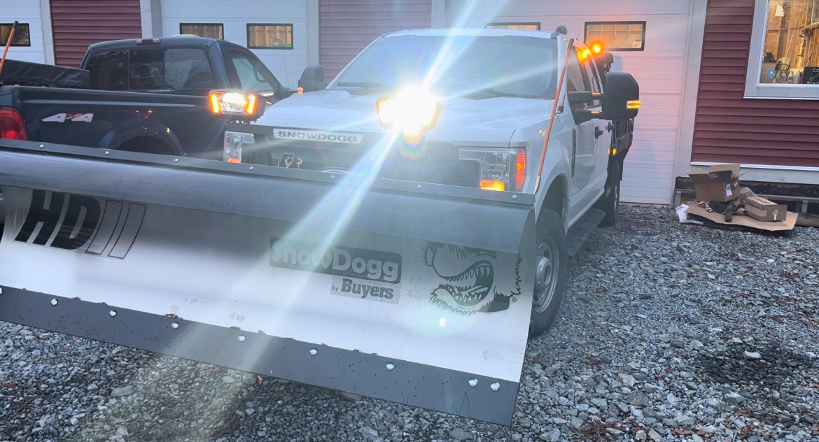 a white truck with a silver plow blade on the front with its lights above the plow on