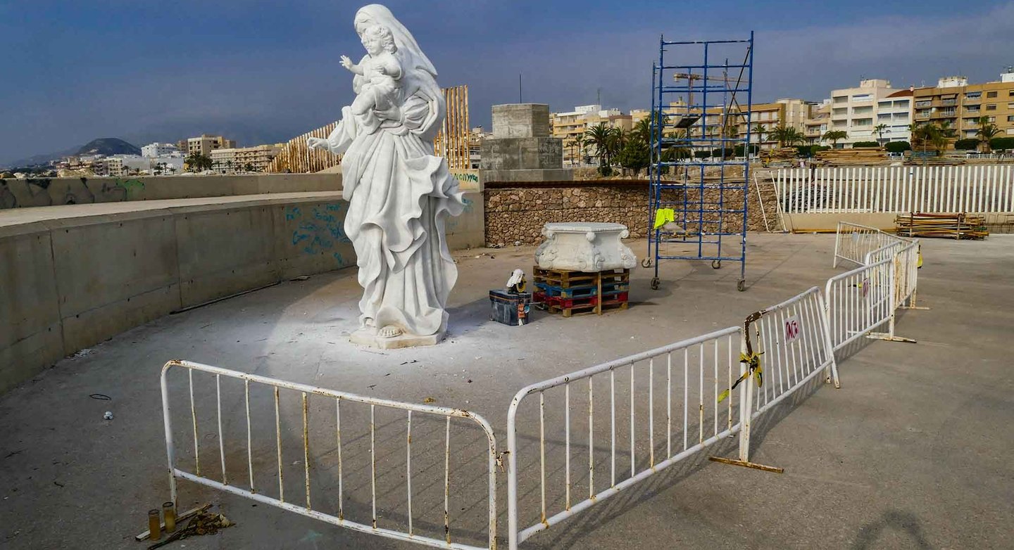 White marble statue of the Virgin Mary and child at a coastal construction site with scaffolding.