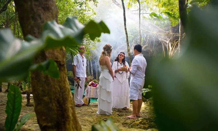 Pareja celebrando una ceremonia de boda maya mística espiritual en un cenote rodeado por la selva maya de la Riviera Maya.