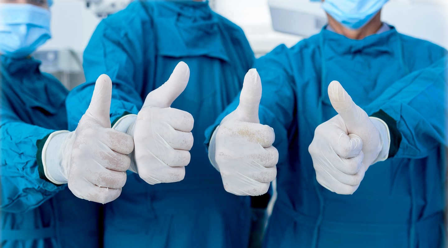 four physicians in gowns and gloves giving the thumbs-up approval sign.