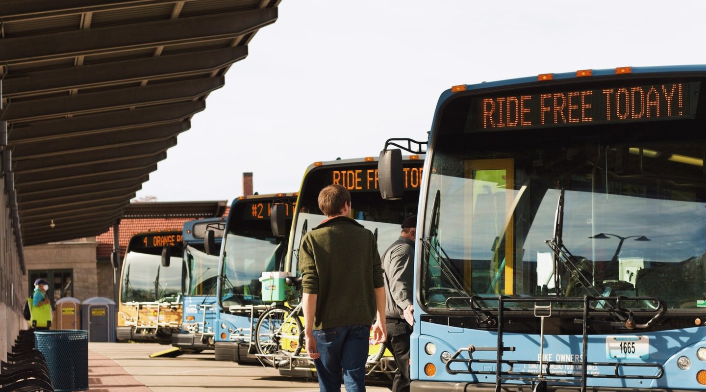 Man walking in front of a line of buses with the bus route sign reading "Ride Free Today"