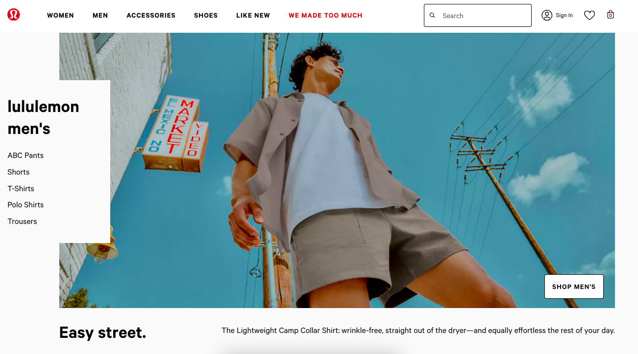A from-below photograph of a man wearing a beige collared shirt, white t-shirt, and beige shorts.