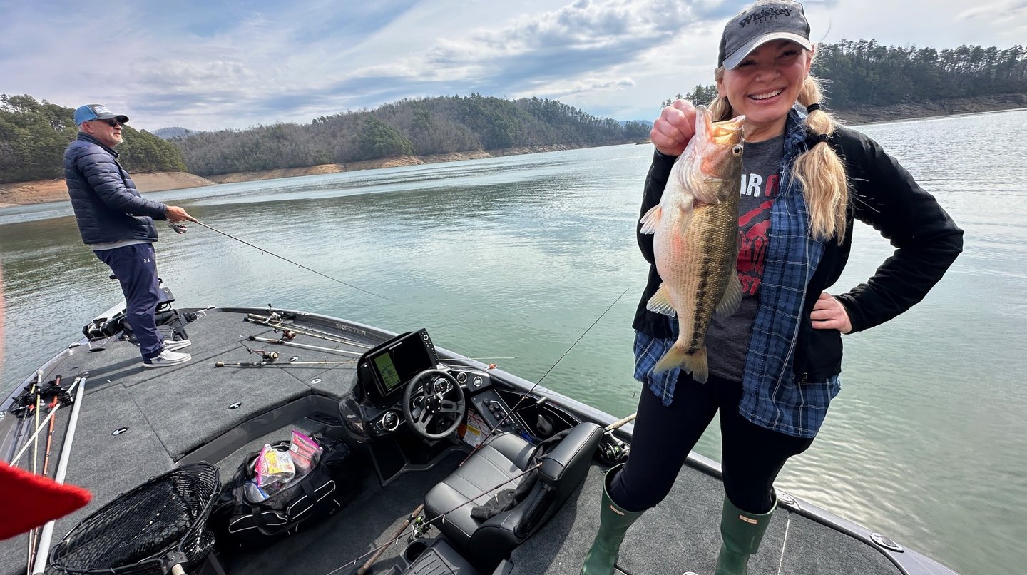  smiling woman holding a bass while fishing