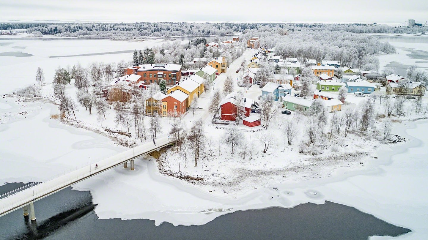Winter aerial view of Pikisaari island in Oulu, featuring historic wooden houses and snowy riverside