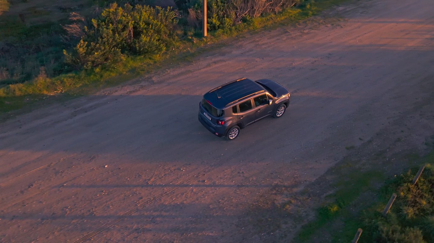 Vue aérienne par drone d’une Jeep Renegade sur un chemin en gravier à la golden hour