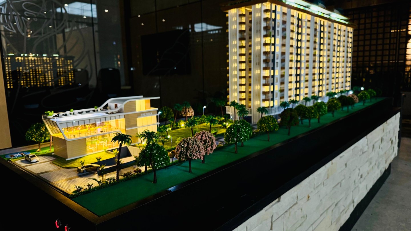 Illuminated architectural scale model of a modern luxury high-rise apartment building and clubhouse.