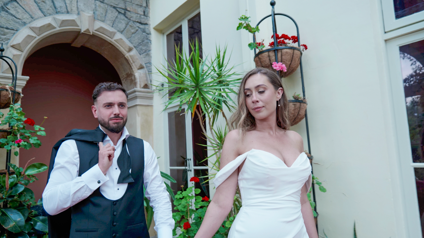 A bride and groom joyfully walking surrounded by floral decorations and smiling guests.