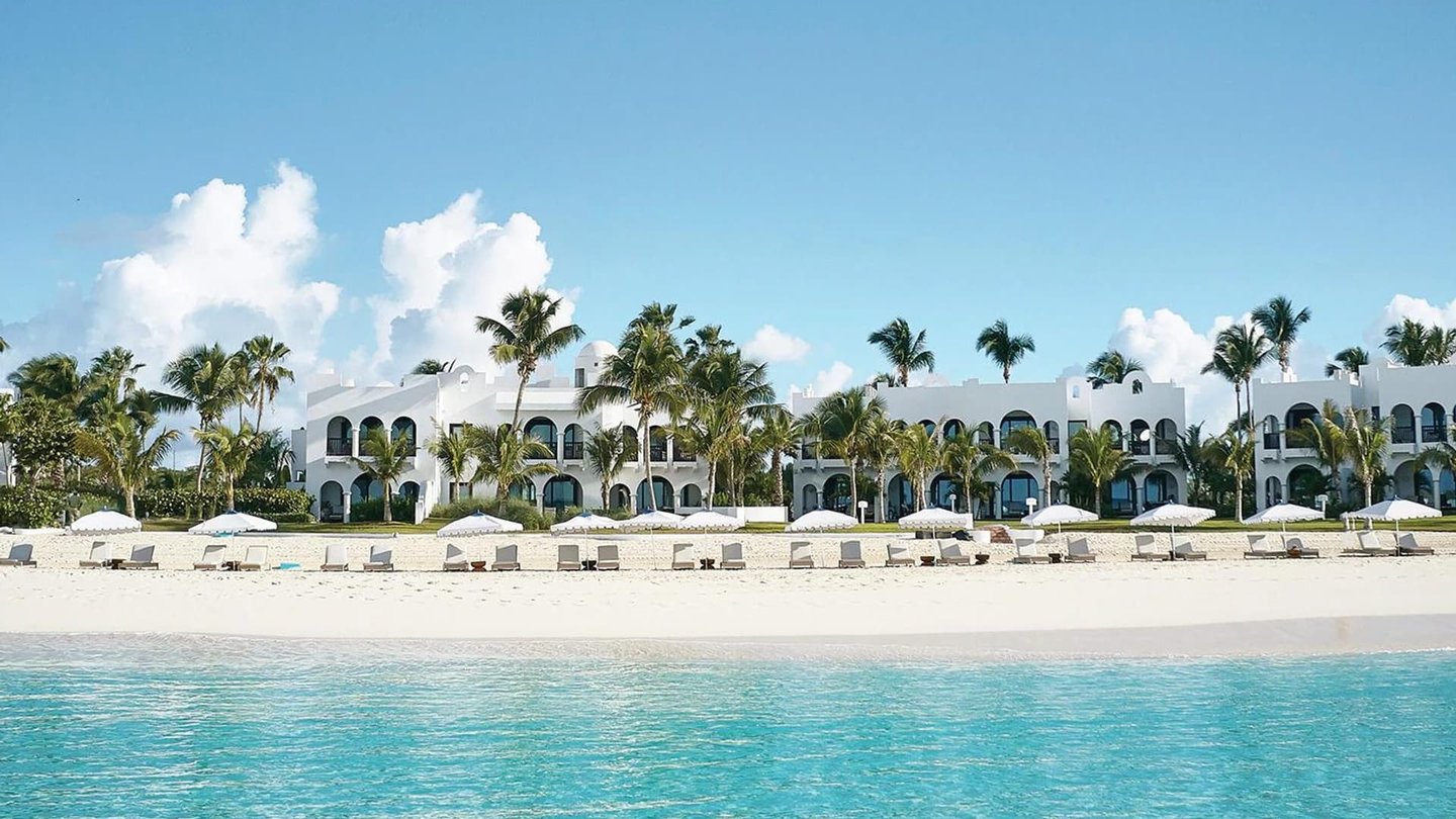Luxury white beachfront resort with palm trees and sun loungers on a tropical white sand beach.
