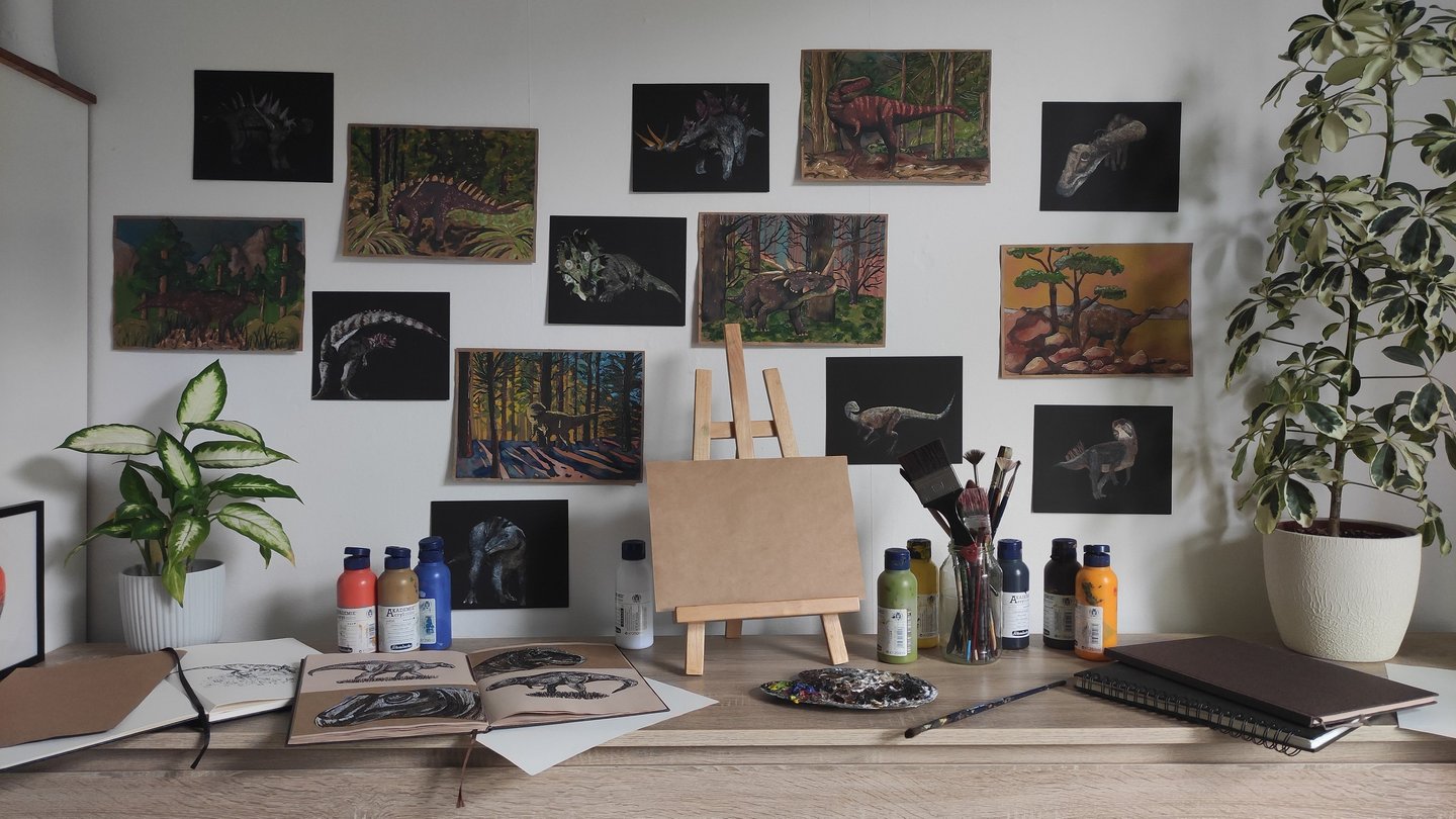 a desk with a painting easel, artworks and a potted plant