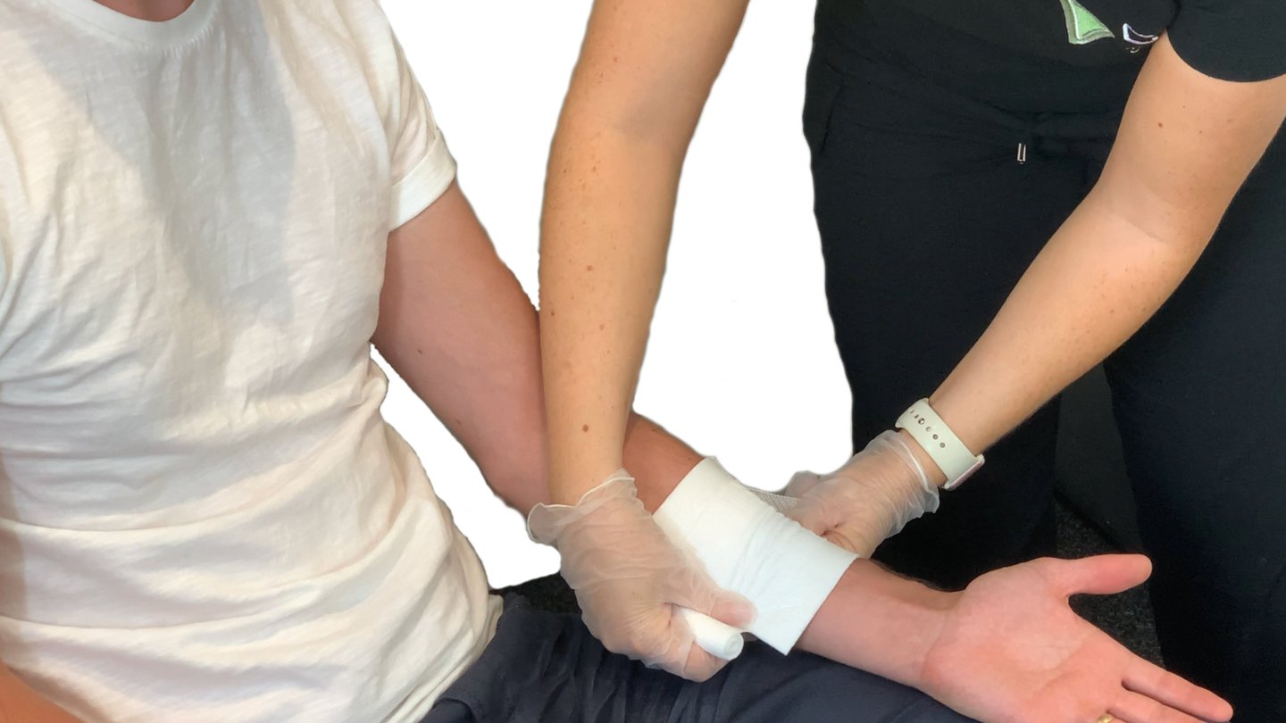 a first aid instructor demonstrating applying a banding on a persons forearm