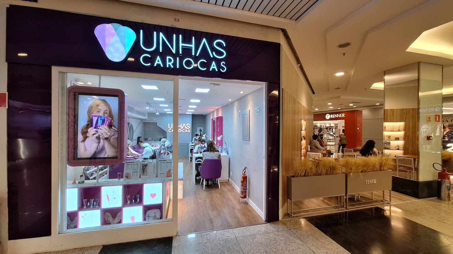 Modern Unhas Cariocas nail salon storefront in a bright shopping mall with professional manicurists.