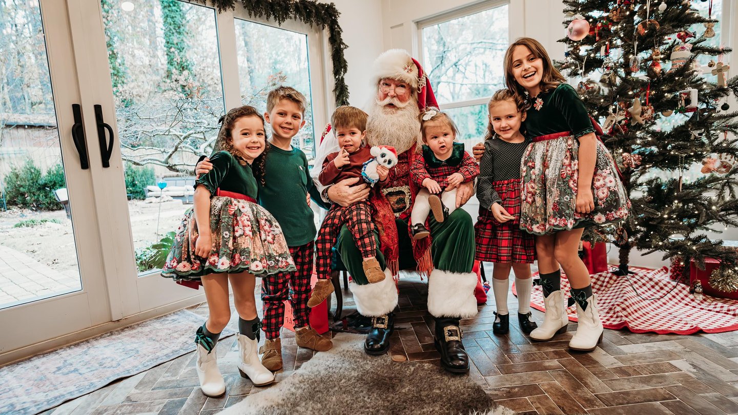 A group of happy children posing with Santa Claus next to a decorated Christmas tree for holiday photos.