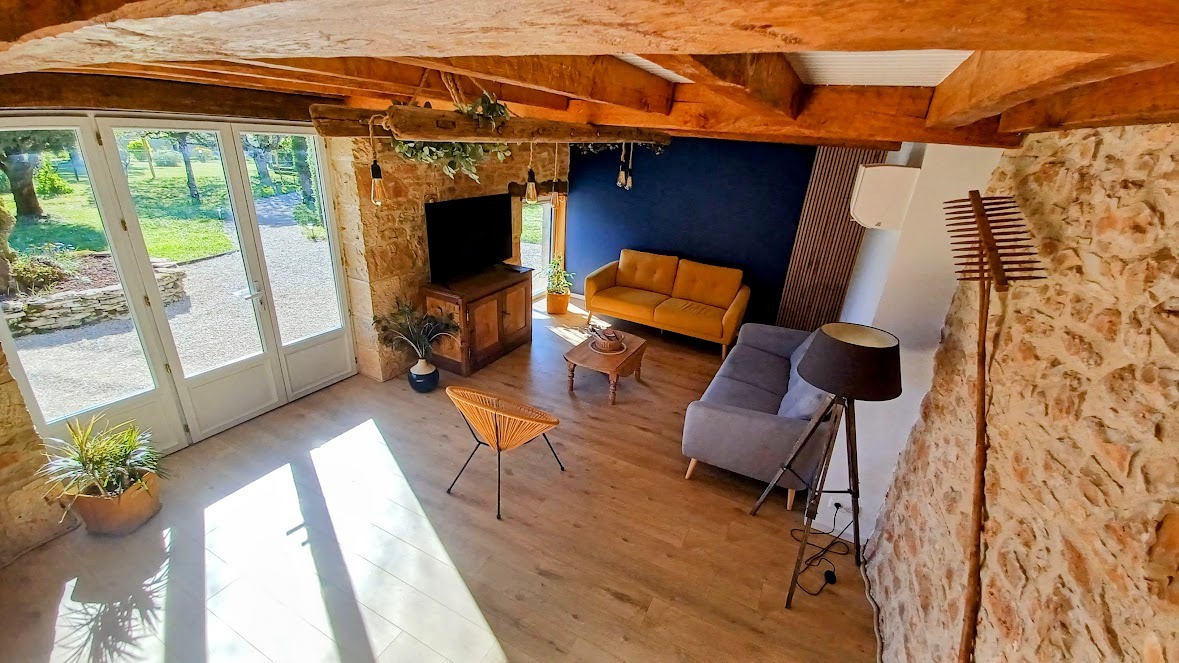 Grand salon de 30 m² avec murs en pierre, poutres apparentes, canapés confortables et télévision