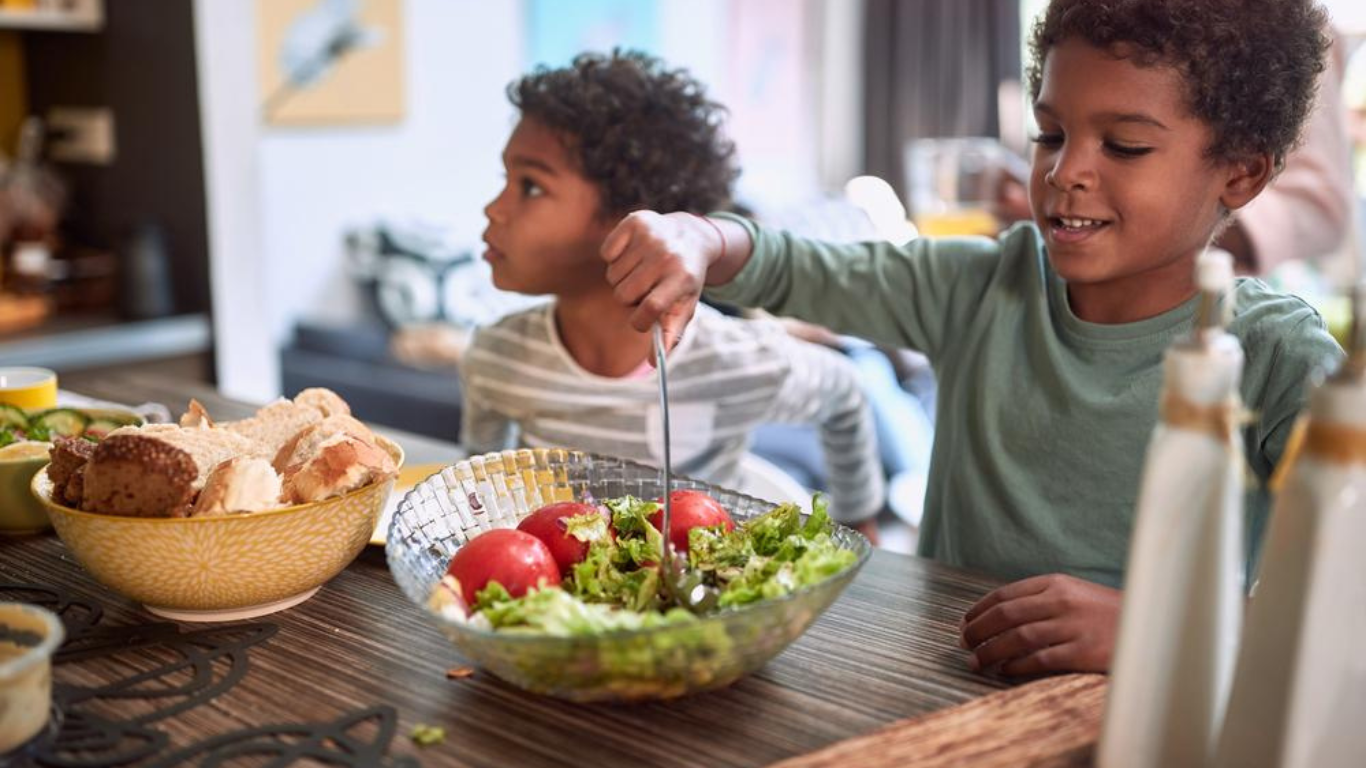 two children eating a salad in a bowl