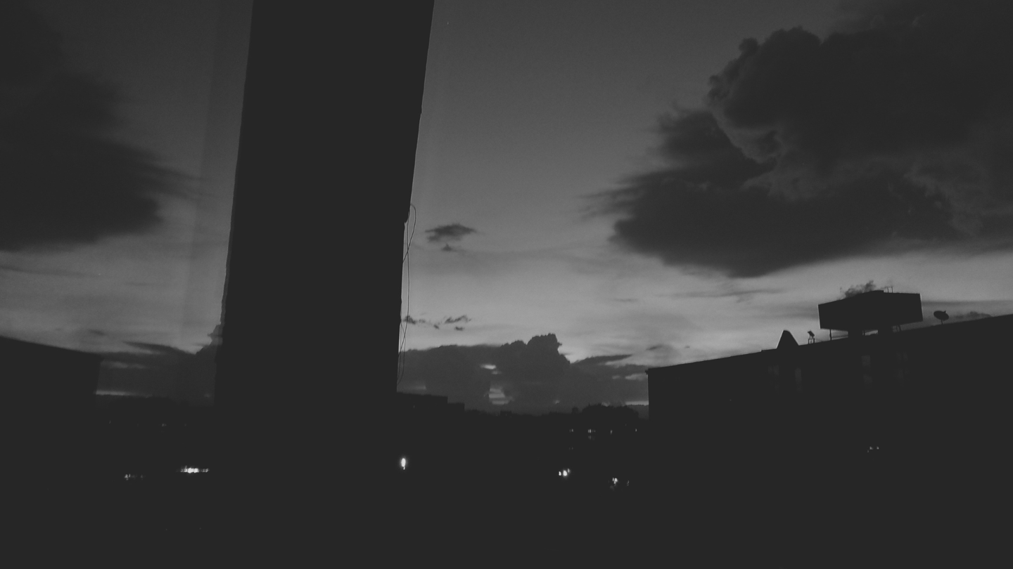 Paisaje urbano nocturno bajo un cielo nublado, con siluetas de edificios que crean una atmósfera.