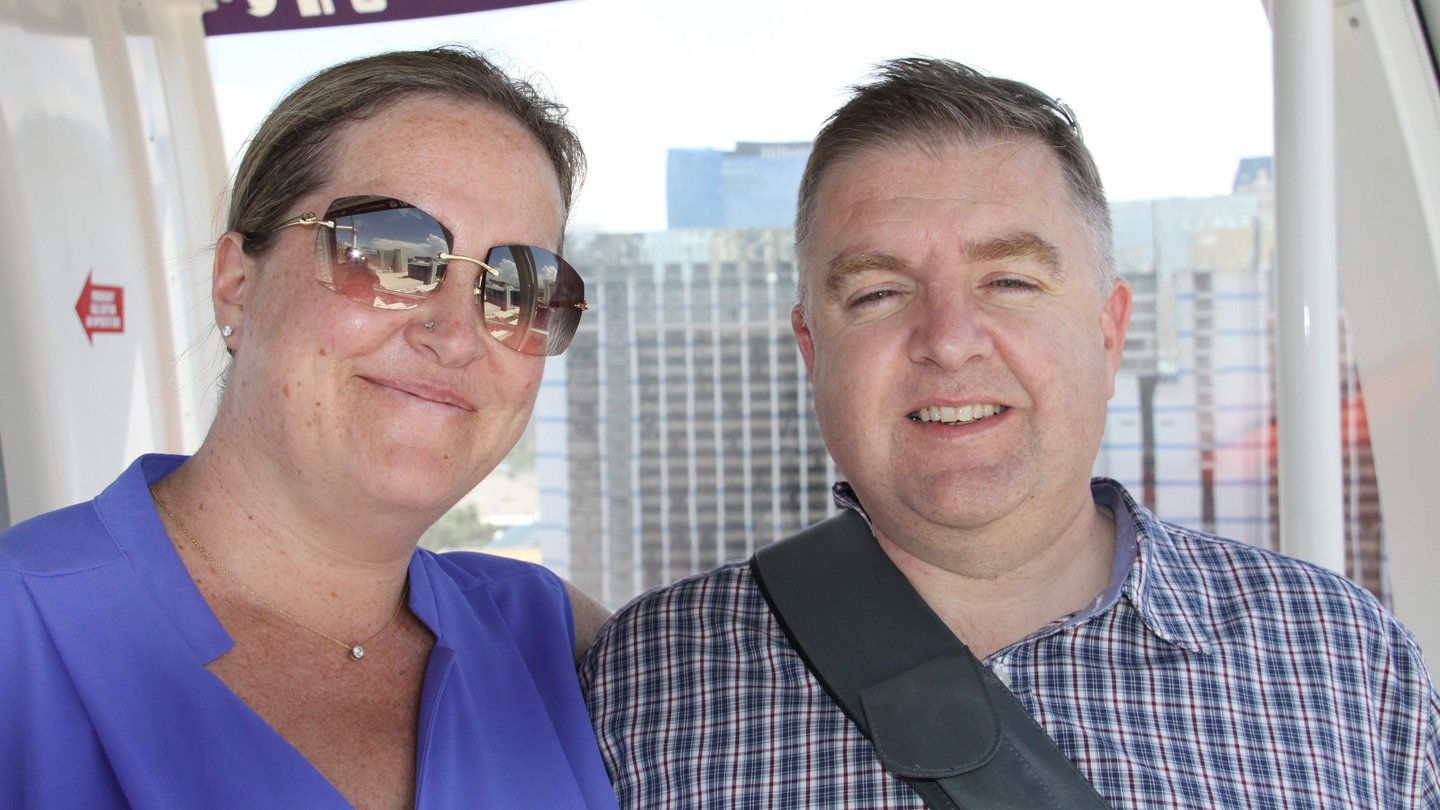 Two adults posing inside observation wheel cabin with city skyline in background, capturing a moment of leisure