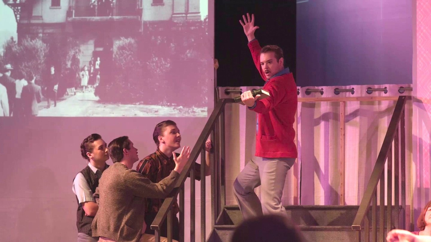 A handsome young man stands in frozen animation on the stairs.