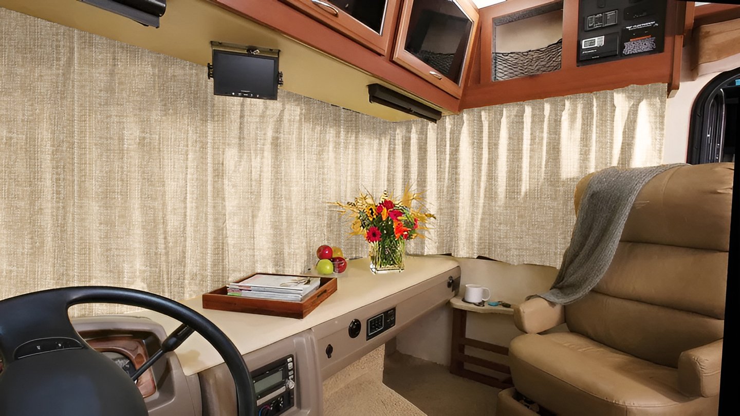 Interior of a luxury RV cockpit featuring beige blackout curtains, a leather swivel chair, and fresh flowers.