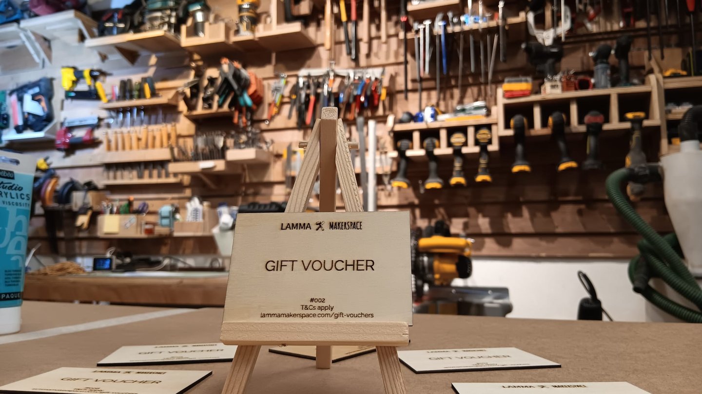 Wooden gift voucher on a miniature easel in a fully equipped Lamma Makerspace workshop.