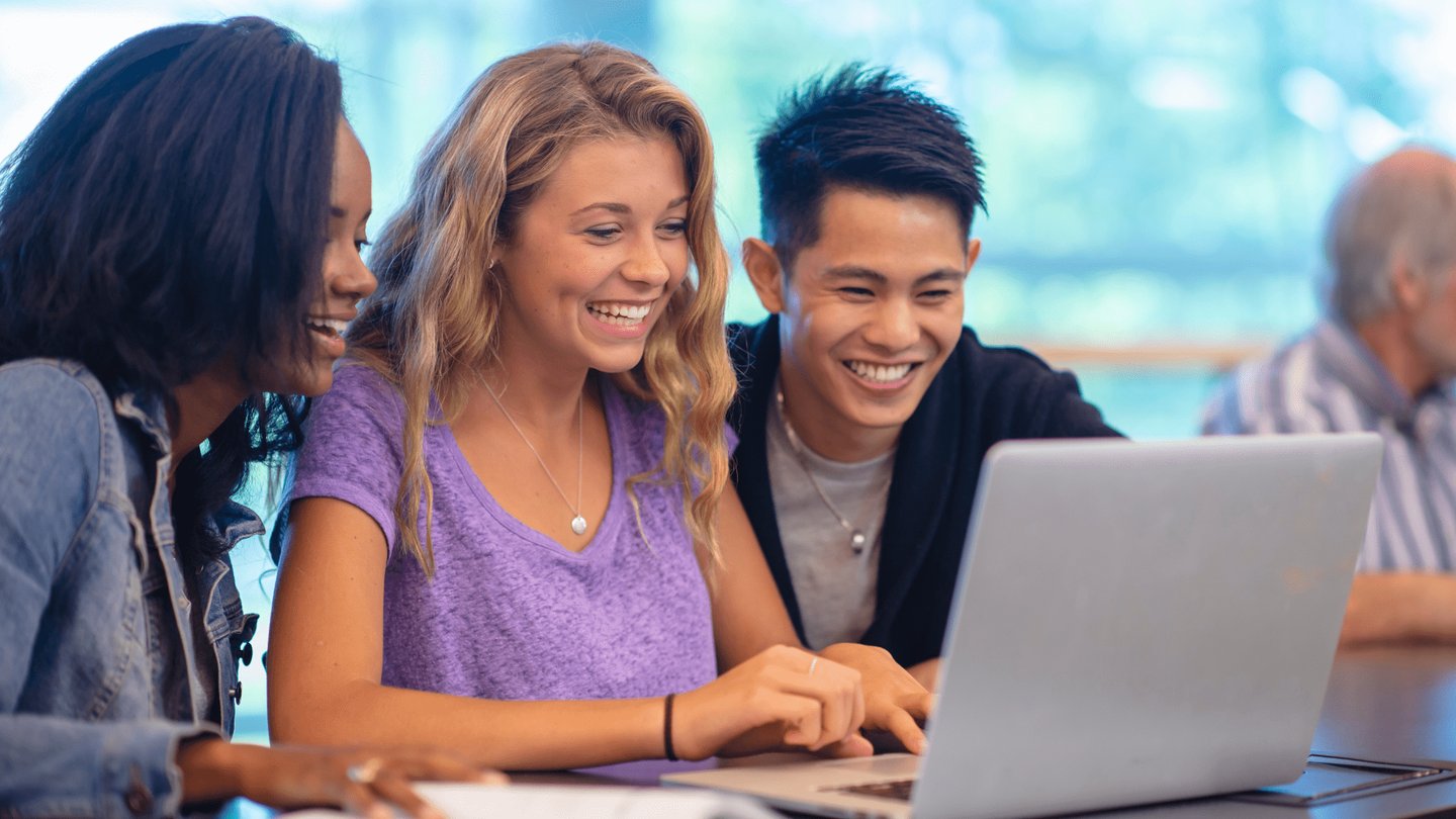 imagem de três jovens reunidos olhando para um computador estudando sobre finanças.