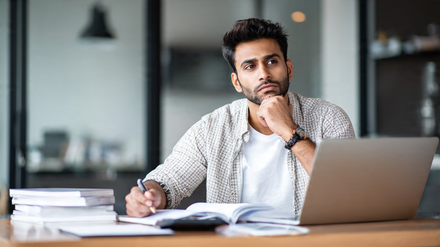 Young male entrepreneur thinking and working on a laptop in a modern office.