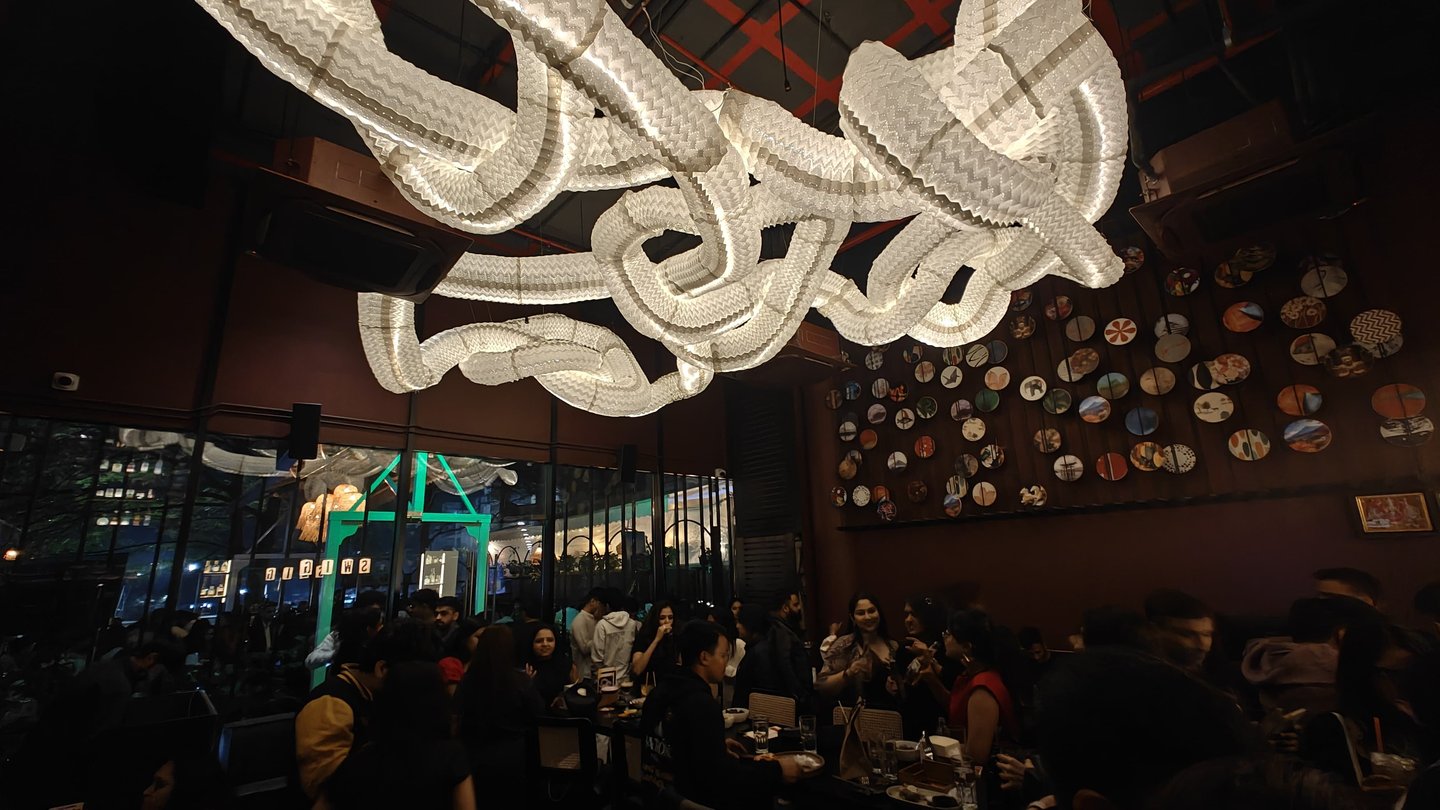 Crowded modern restaurant interior featuring a large wavy paper lantern light fixture and decorative plate wall art.