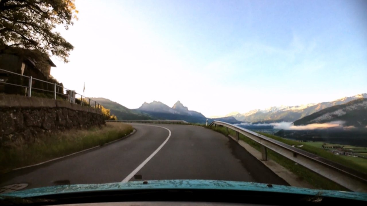 Winding mountain road with a view of the Swiss Alps during a scenic summer car drive.