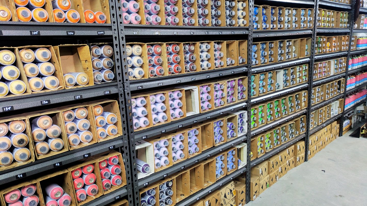 Shelves of colorful spray paint cans organized by color in HAVRE's studio.