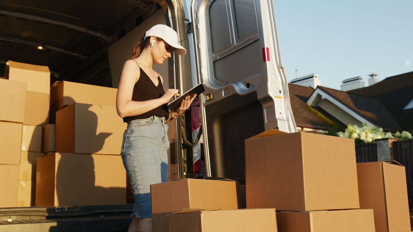 Woman checking inventory after unloading cardboard boxes from van