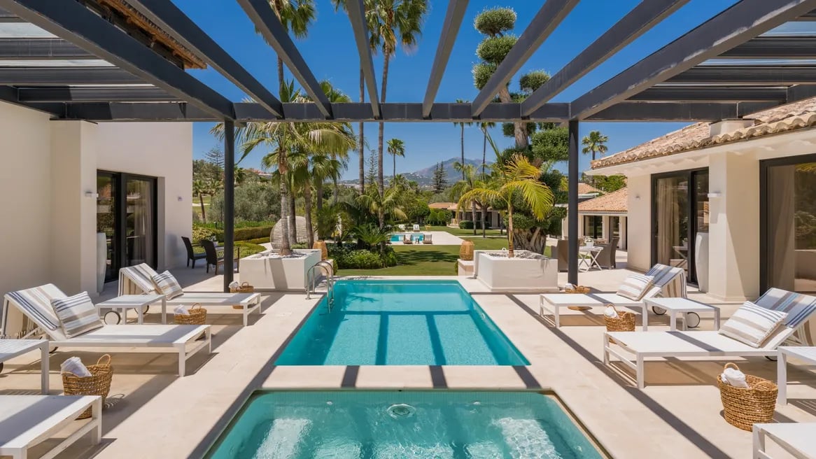 Guest heated pool surrounded by terraces and palm gardens at Villa El Olivo, Marbella