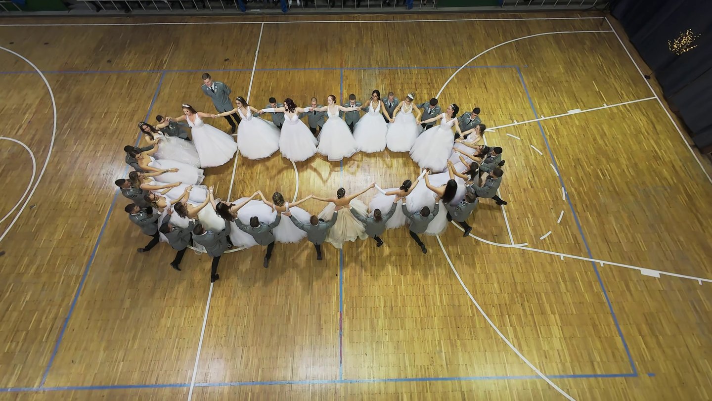 beltéri FPV drónos kép egy sportcsarnokban rendezett szalagavató bálról ahol ovális formában táncol