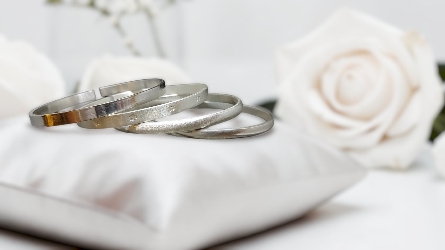 Elegant stack of 999 fine silver bangles on a white satin pillow with roses.