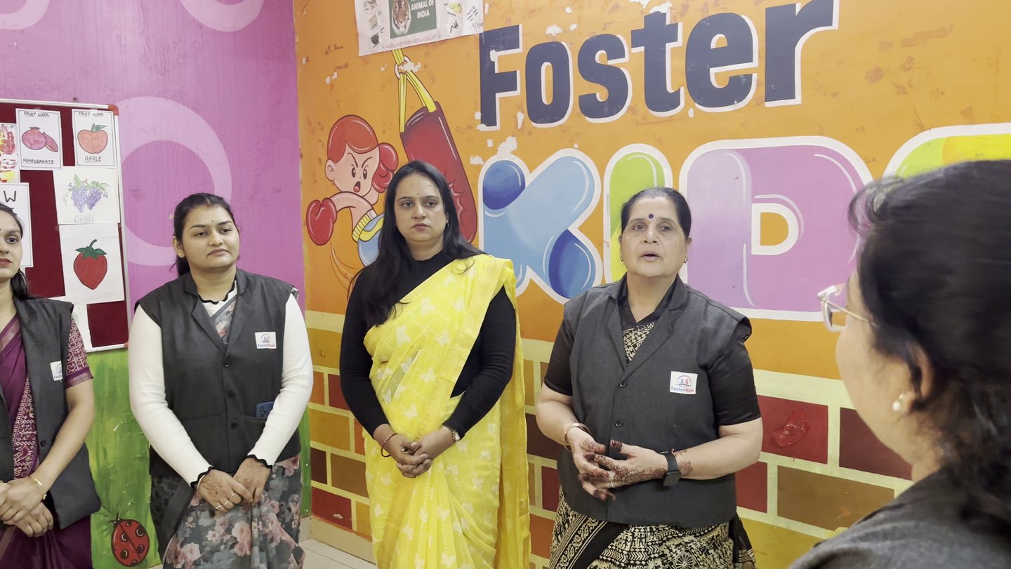 Preschool teachers at Foster Kids play school standing in a classroom with educational wall charts.