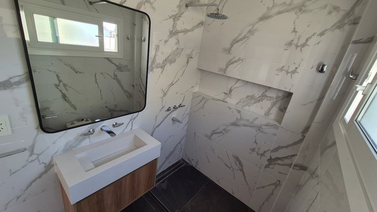 Modern bathroom featuring white marble wall tiles, a floating vanity with a wooden cabinet, and a walk-in shower.