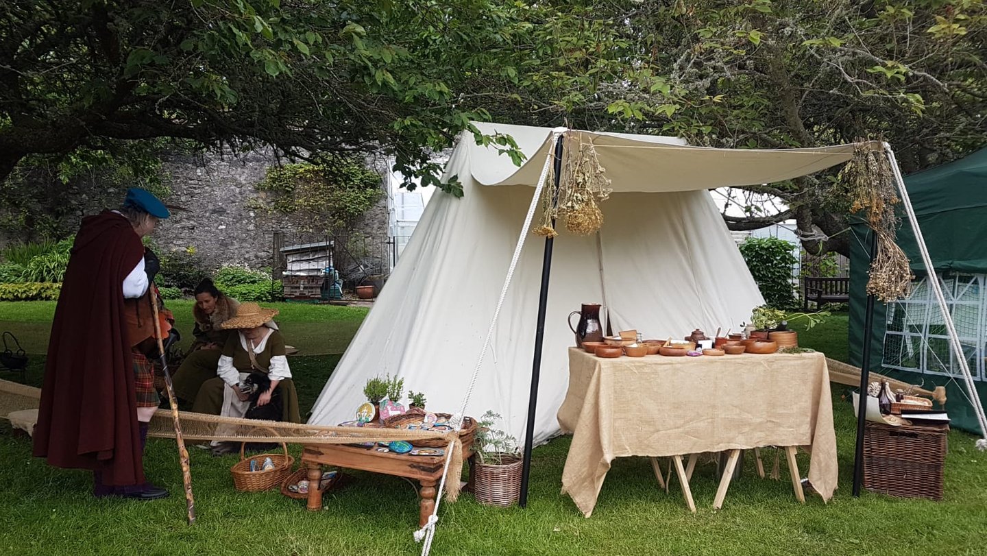 reenactors talking beside a medieval tent with a table of herbal remedies