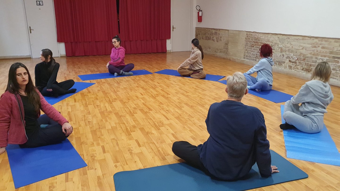 a group of people sitting on yoga mats in a circle, classe di esercizi di bioenergetica