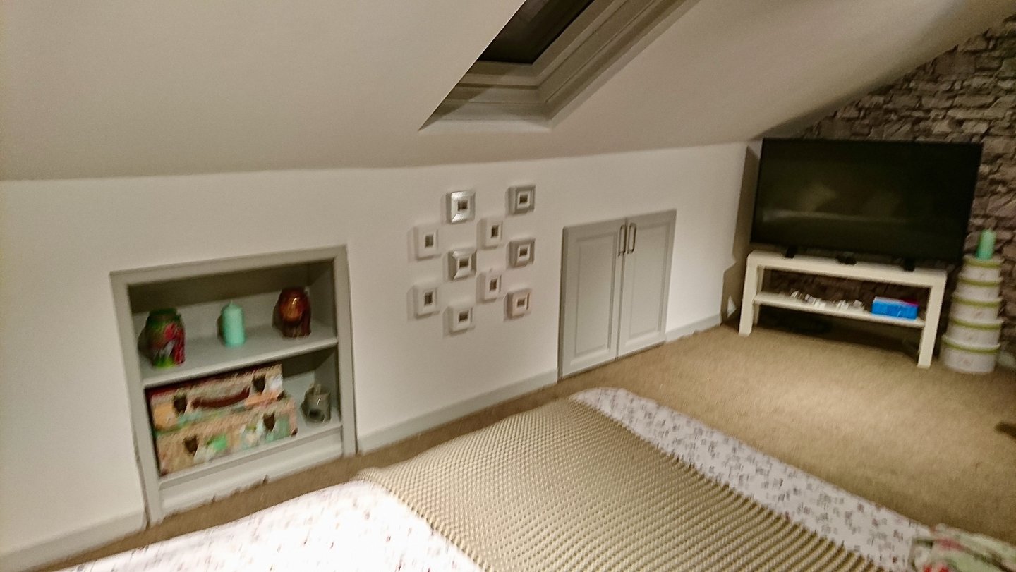 Cozy attic bedroom with sloped ceilings, built-in shelving, wall art, and a flat-screen TV.