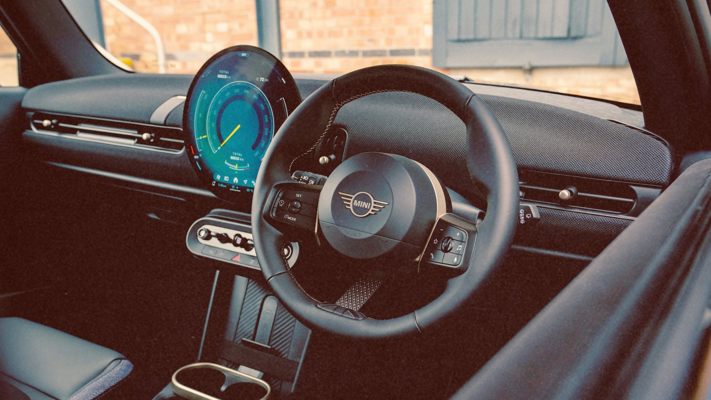 Modern interior of a Mini Cooper featuring a round digital dashboard and leather steering wheel.
