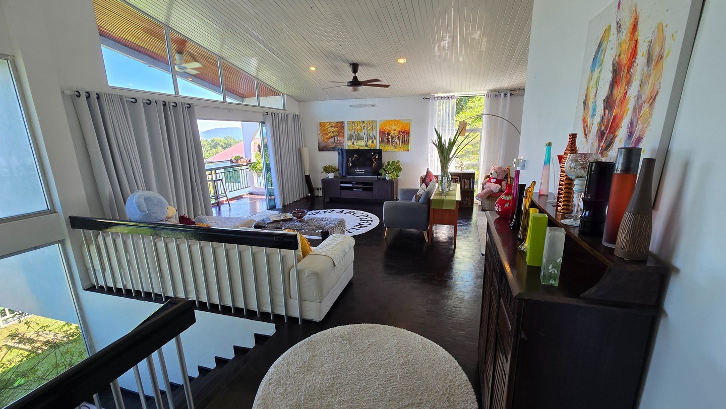 Modern bright living room interior with white vaulted ceilings, sliding balcony doors, and colorful wall art.