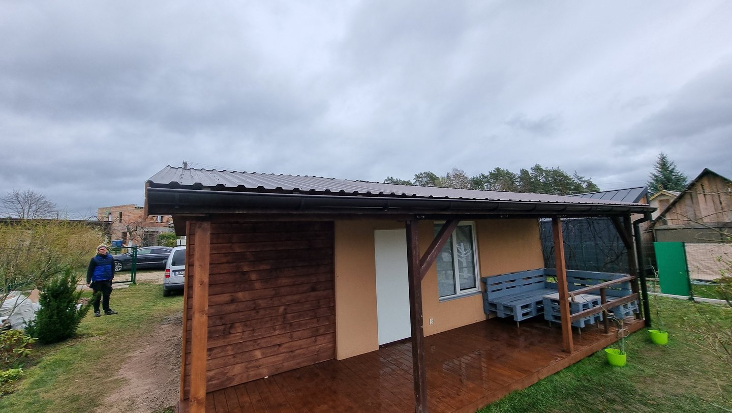 sodo namelis, prie kurio yra termo medienos terasa, sandėliukas malkoms susidėti ir stogas