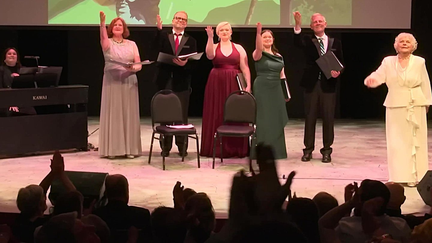 A group of singers in formal attire taking a bow on stage a the end of a live musical performance.