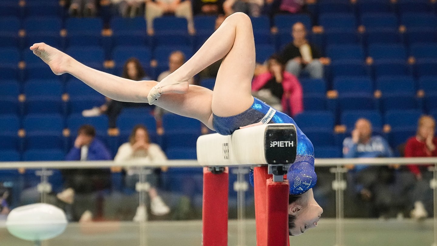 Gymnast performing a balancing routine on a balance beam during a gymnastics competition.