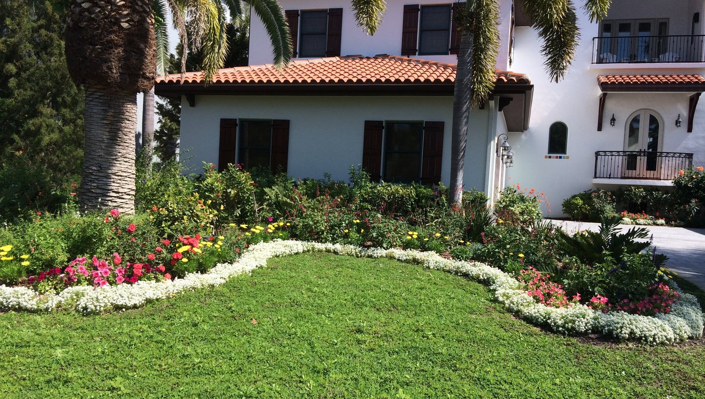 Stucco home with wrap around white flowers and another layer of colored flowers behind it.