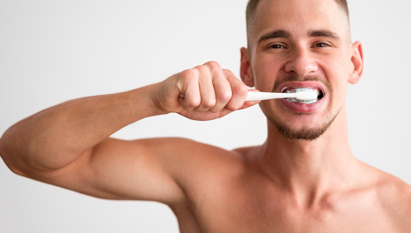 A man brushing his teeth with a white toothbrush and toothpaste for daily oral hygiene.