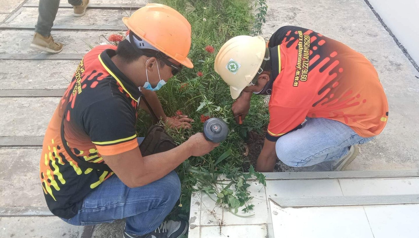 Two professional pest control technicians in hard hats inspecting a garden for termite activity.